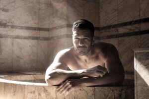Muscular man enjoying a serene moment in a marble sauna with soft light effects.